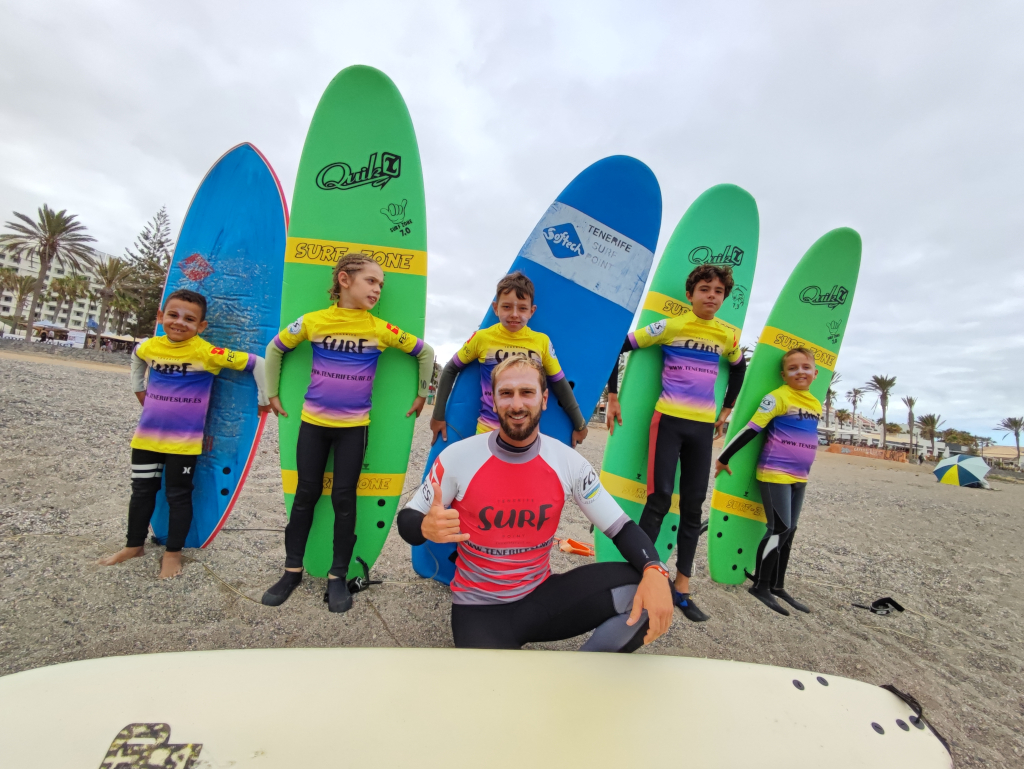 Surflehrer mit Kindern, die Bretter am Strand von Teneriffa halten.