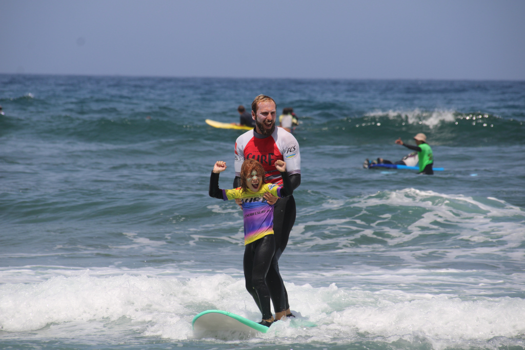 Erwachsener und kindlicher Surfer im Surfunterricht an einem Strand auf Teneriffa.