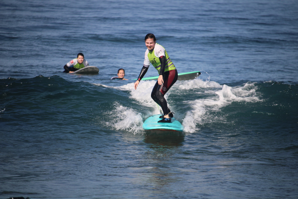 Surfer, der auf einer Welle in Punta del Hidalgo, Teneriffa, reitet, mit zwei Personen im Hintergrund.
