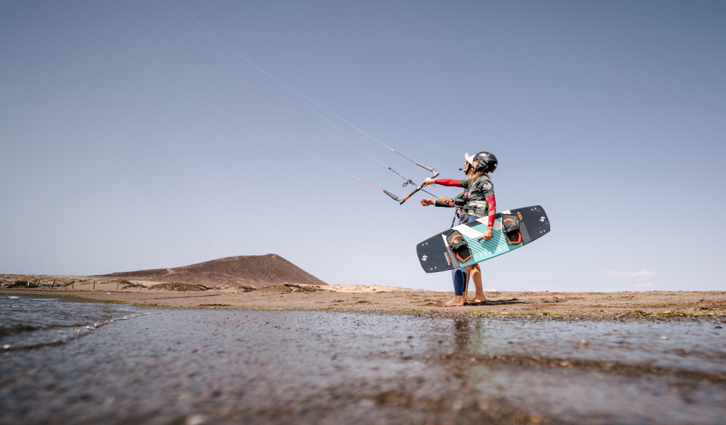 Person, die Kitesurfen in Playa El Médano, Teneriffa, praktiziert, mit einem Hügel im Hintergrund.
