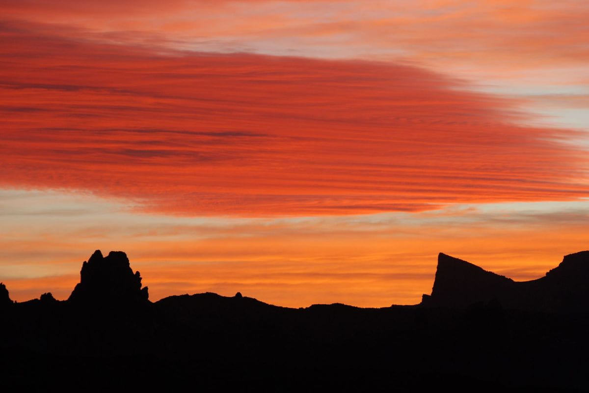 Sonnenuntergang über Bergen auf Teneriffa mit roten Wolken und orangefarbenem Himmel.