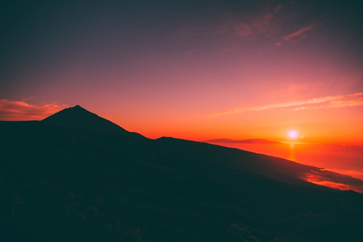 Sonnenaufgang über dem Teide auf Teneriffa mit rotem Himmel und Sonne am Horizont.