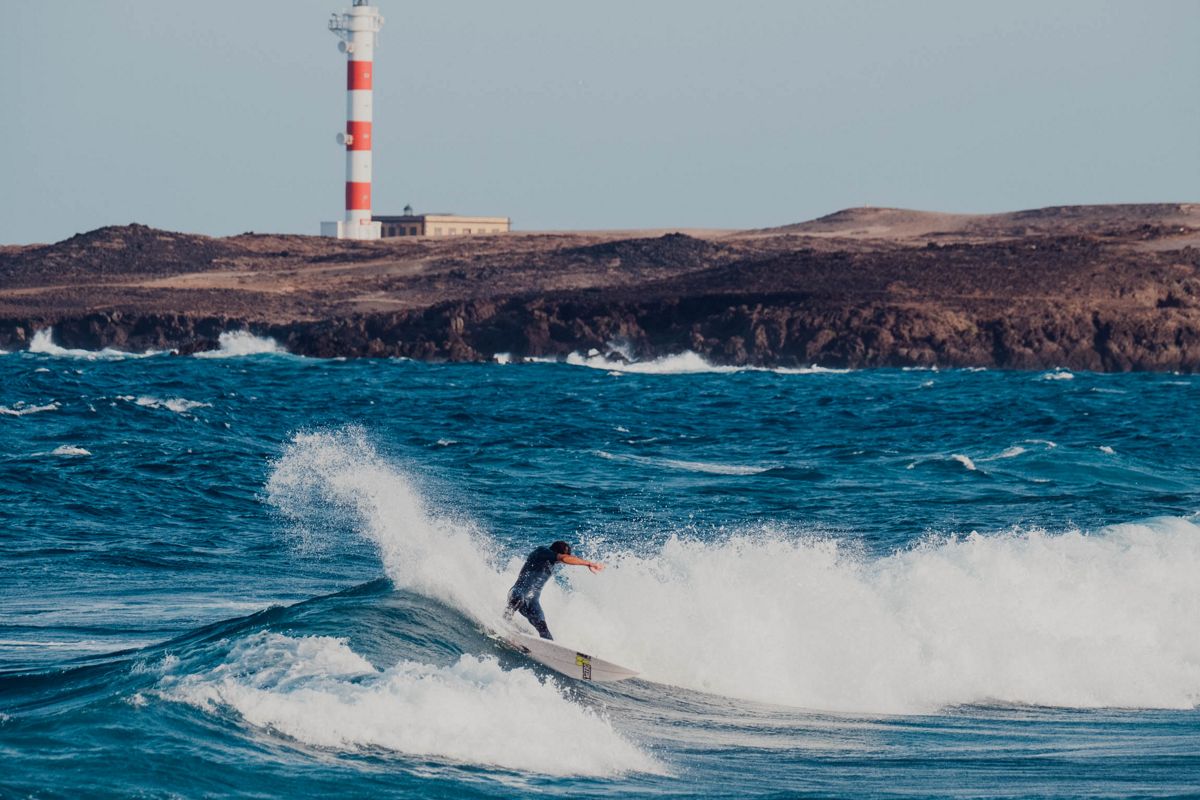 Surfer, der vor dem Leuchtturm in Punta de Hidalgo, Teneriffa, eine Welle reitet.