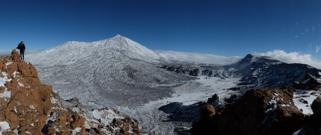 Schneebedeckte Landschaft des Berges Teide auf Teneriffa mit einem Wanderer auf einem Felsen.