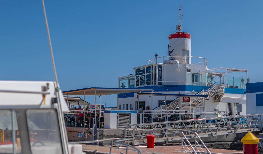 Weiß-blaues Gebäude mit rotem Leuchtturm in Santa Cruz de Tenerife, gesehen von einem Pier aus.