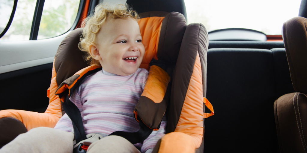 Kind, das in einem Kindersitz im Auto lächelt.