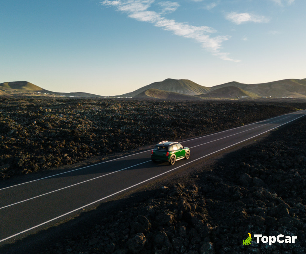 Grünes Auto fährt auf der Straße zwischen vulkanischen Landschaften auf Teneriffa. TopCar-Logo.