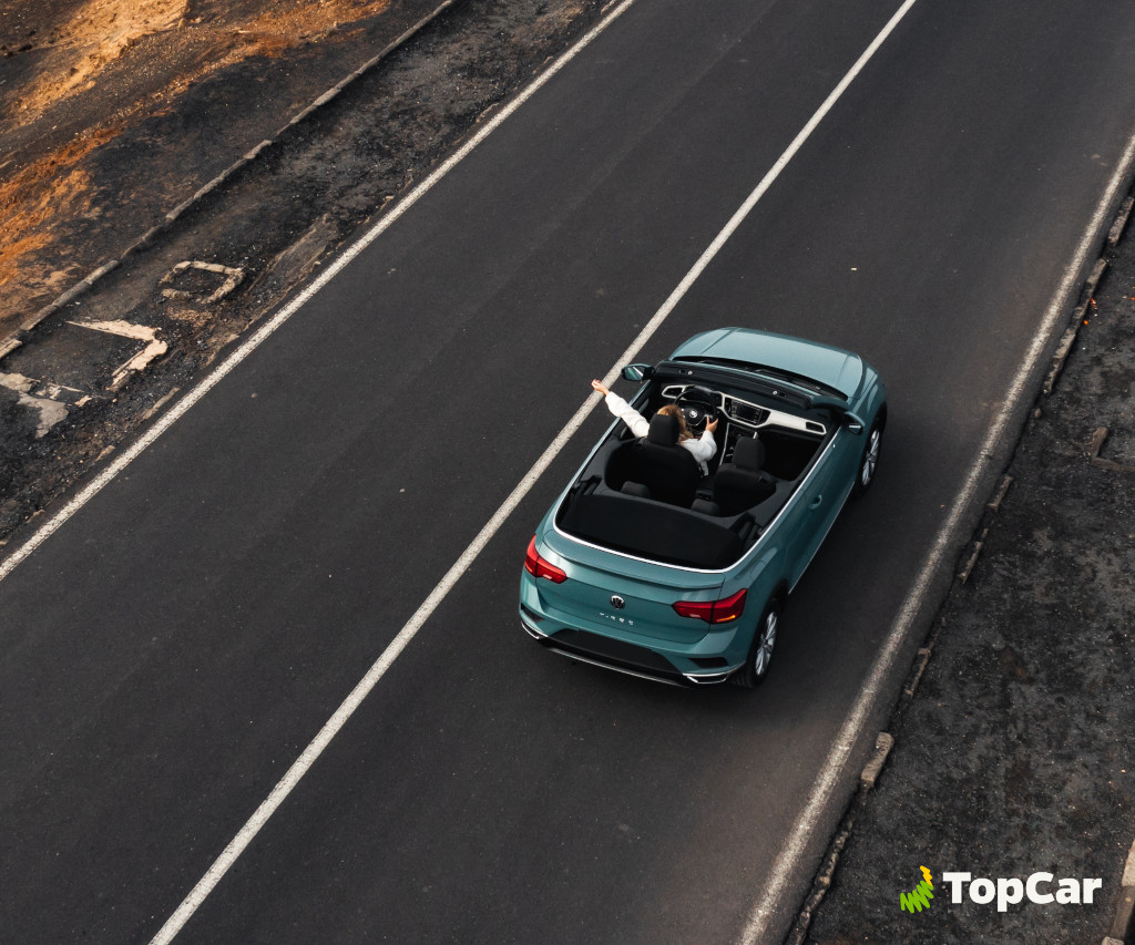 Person, die ein blaues Cabrio auf der Straße auf Teneriffa fährt. Sichtbarer Text: TopCar.