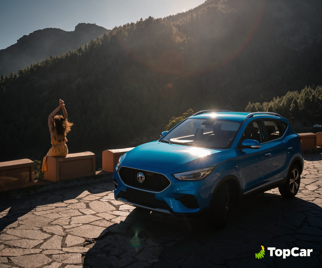 Blaues Auto vor Bergen auf Teneriffa, Frau sitzt an der Wand unter der Sonne.