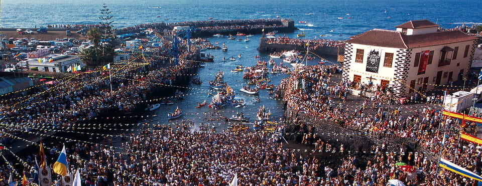 Menschenmengen feiern im Hafen von Puerto de la Cruz auf Teneriffa mit Booten und Gebäuden.