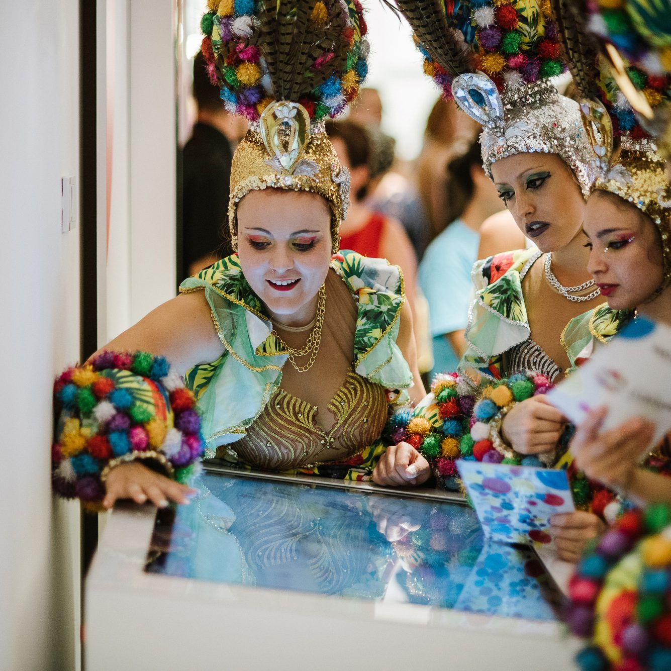Menschen in bunten Karnevalskostümen interagieren auf Teneriffa mit einem Touchscreen.