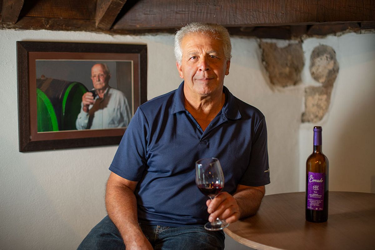 Mann hält ein Glas Wein neben Flasche und Porträt in der Cantina auf Teneriffa.