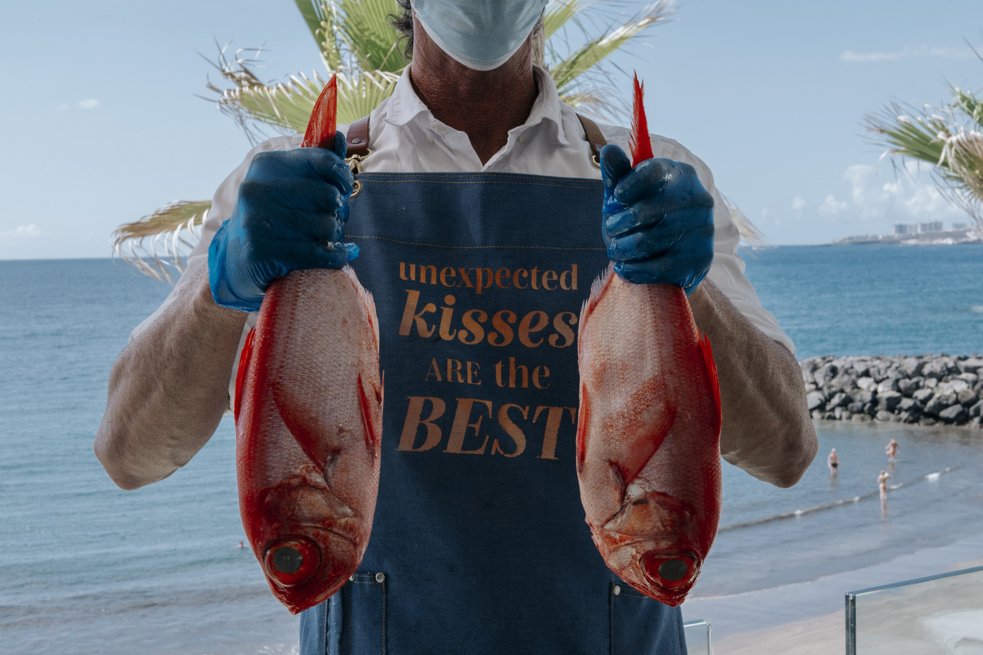 Person, die zwei Fische mit Schürze hält und sagt, unerwartete Küsse seien die besten auf Teneriffa.