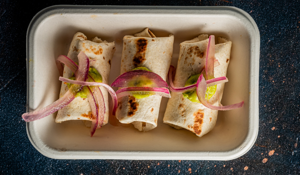 Drei Burritos mit roten Zwiebeln und Salsa Verde auf einem rechteckigen Teller auf Teneriffa.