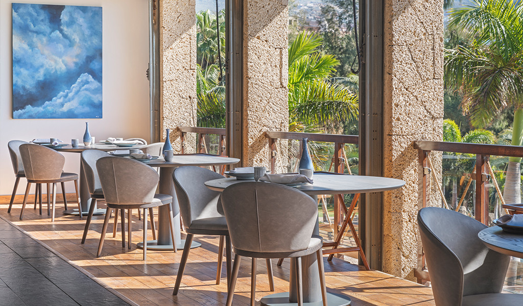 Speisesaal mit Tischen und Stühlen neben großen Fenstern mit Blick auf die Gärten auf Teneriffa.