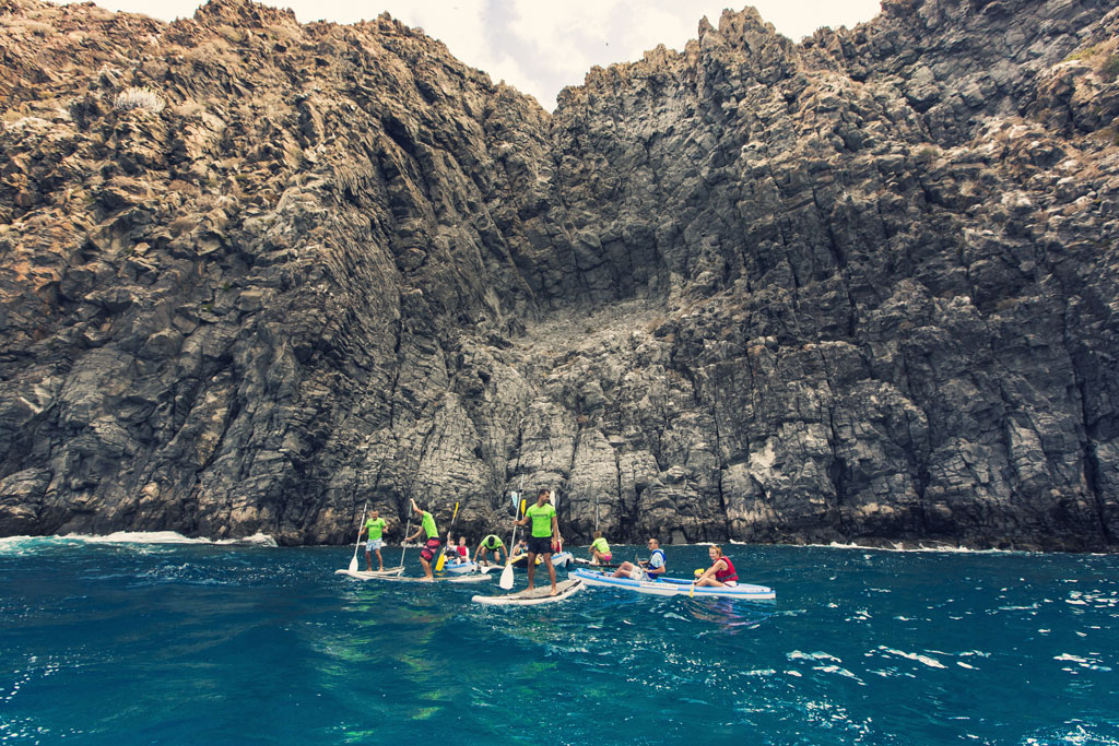 Menschen paddeln vor Klippen auf Teneriffa beim Surfen.