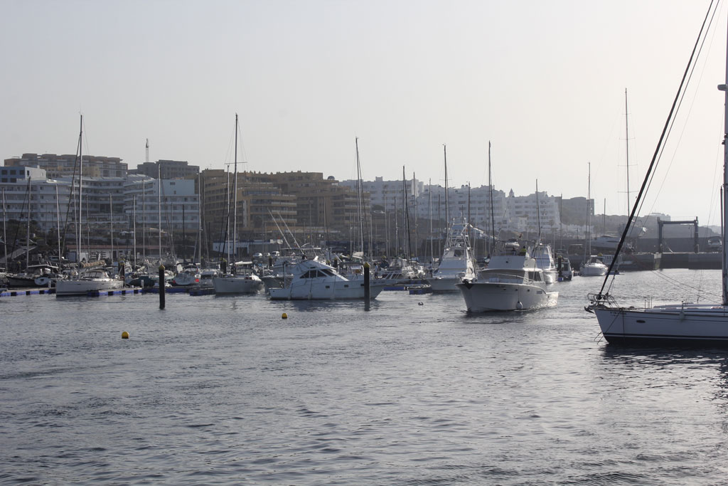 Boote im Hafen von Los Cristianos, Teneriffa, mit Gebäuden im Hintergrund.