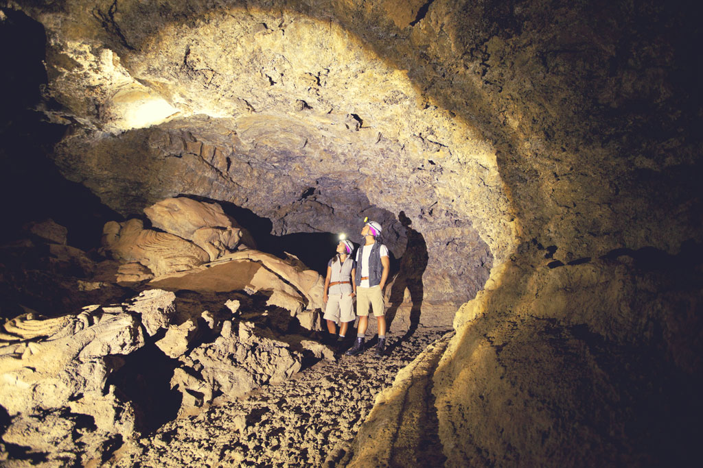 Menschen, die eine Vulkanhöhle auf Teneriffa mit Helmen und Taschenlampen erkunden.