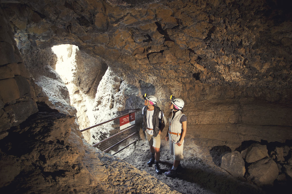 Zwei Personen mit Helmen erkunden eine Höhle auf Teneriffa, in der natürliches Licht hereinströmt.