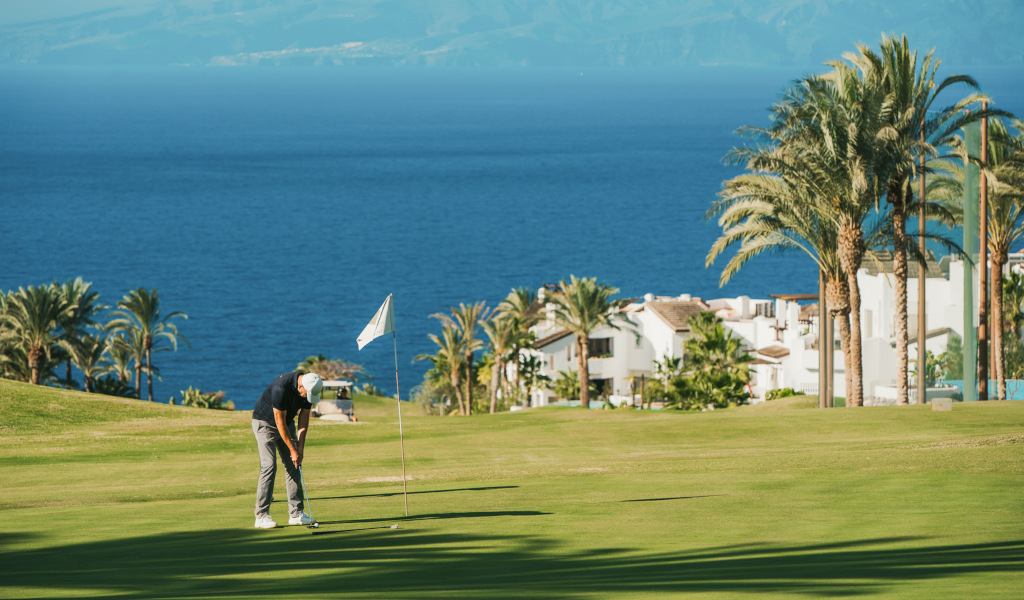 Person, die Golf auf einem Platz mit Meerblick und Häusern auf Teneriffa spielt.