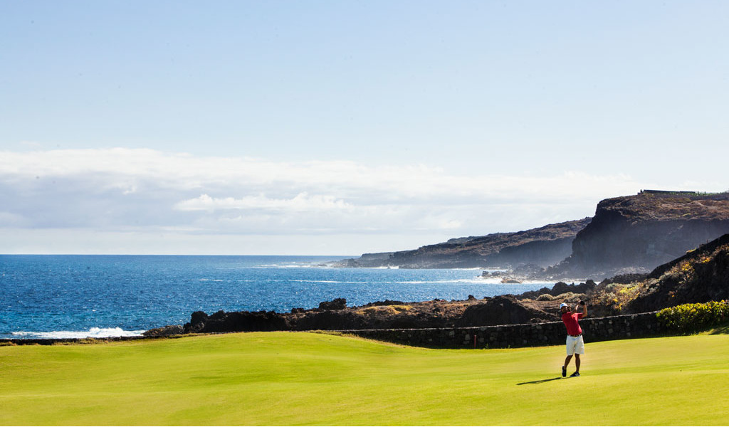 Eine Person, die Golf in der Nähe der Küste auf Teneriffa spielt, mit dem Meer im Hintergrund.