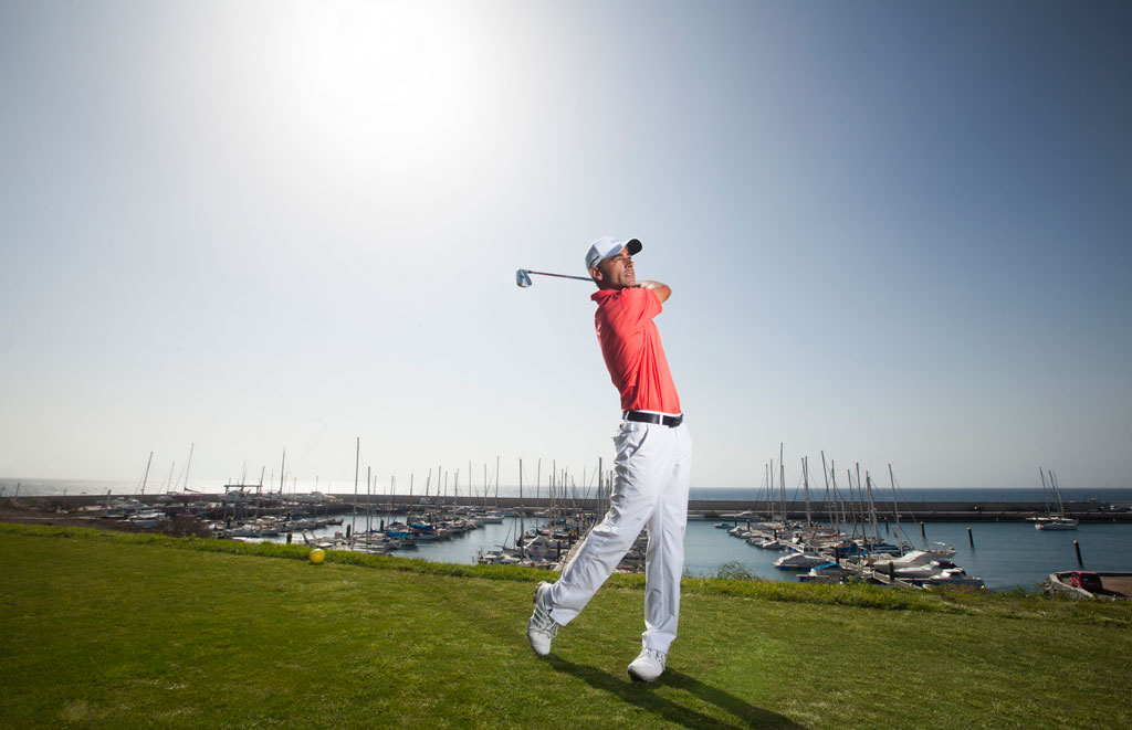 Golfer beim Abschlag mit Yachthafen und Booten im Hintergrund auf Teneriffa.