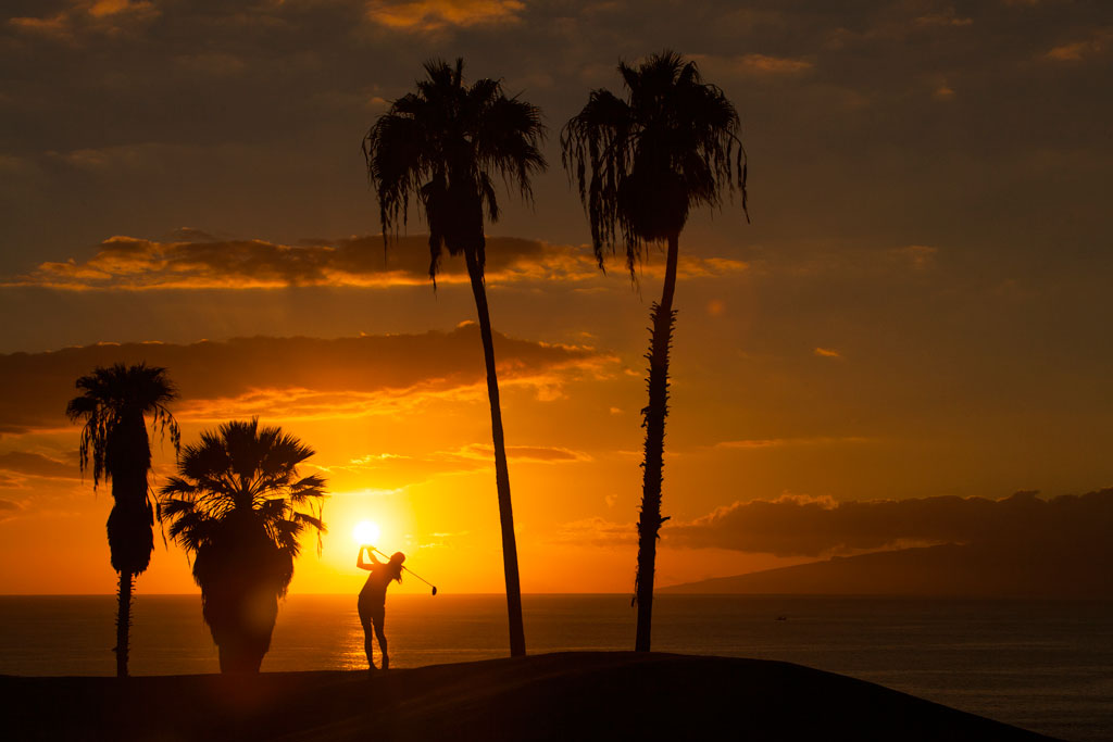 Sonnenuntergang mit Palmen und einer Person, die Golf auf Teneriffa spielt.