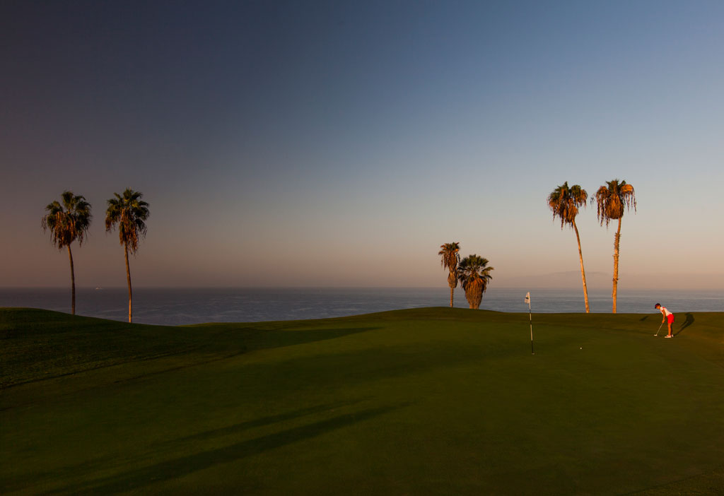Golfplatz bei Sonnenuntergang mit Palmen und Spieler auf Teneriffa.