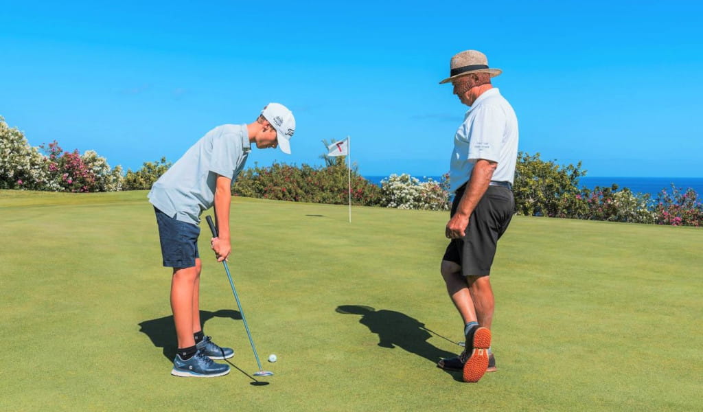 Kind spielt Golf mit einem Erwachsenen im Hintergrund, Teneriffa.
