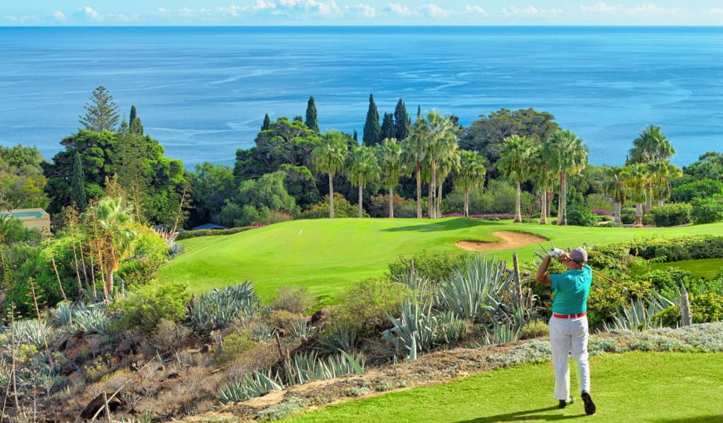 Golfspieler auf einem Platz nahe dem Meer auf Teneriffa, umgeben von Grün und Palmen.