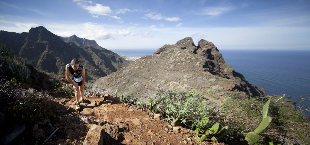 Der Mensch, der auf Teneriffa einen Hügel mit Ausblick auf das Meer und die Berge besteigt.