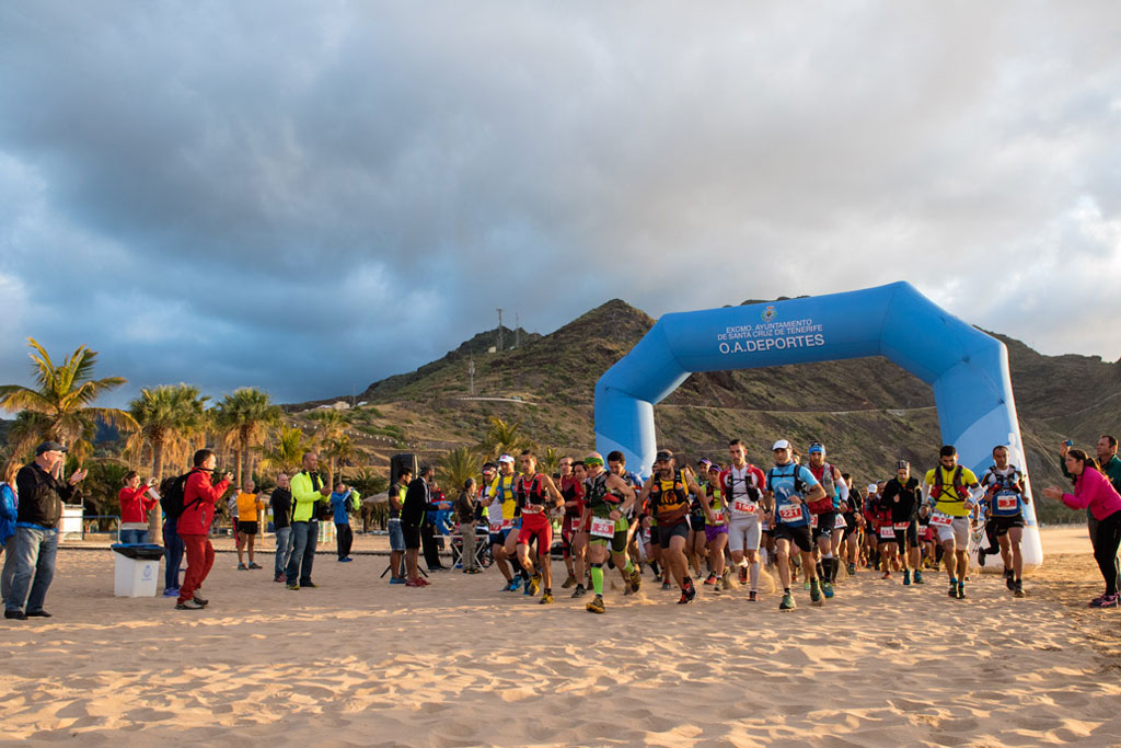 Läufer, die einen Marathon am Strand Las Teresitas auf Teneriffa unter einem blauen Bogen starten.