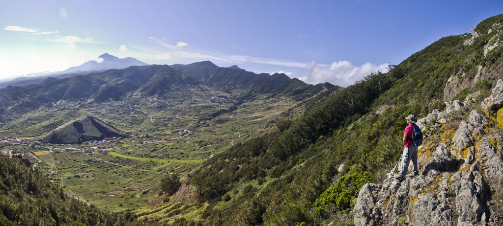 Person, die ein bergiges Tal auf Teneriffa beobachtet, Panoramablick auf Berge und grüne Felder.