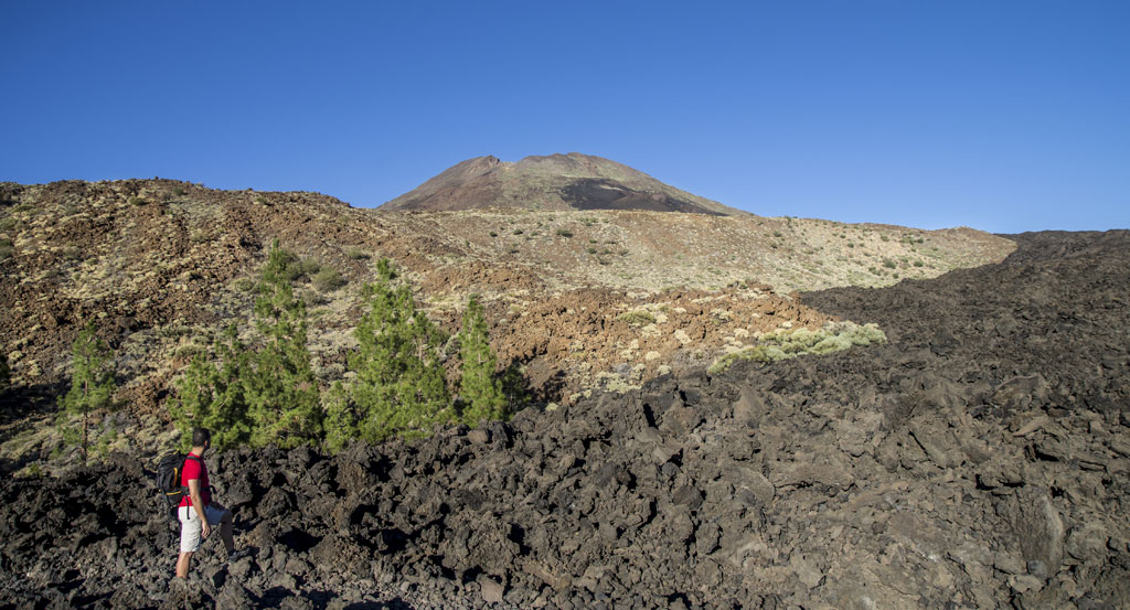 Person, die in einer vulkanischen Landschaft mit dem Berg Teide im Hintergrund auf Teneriffa spaziert.