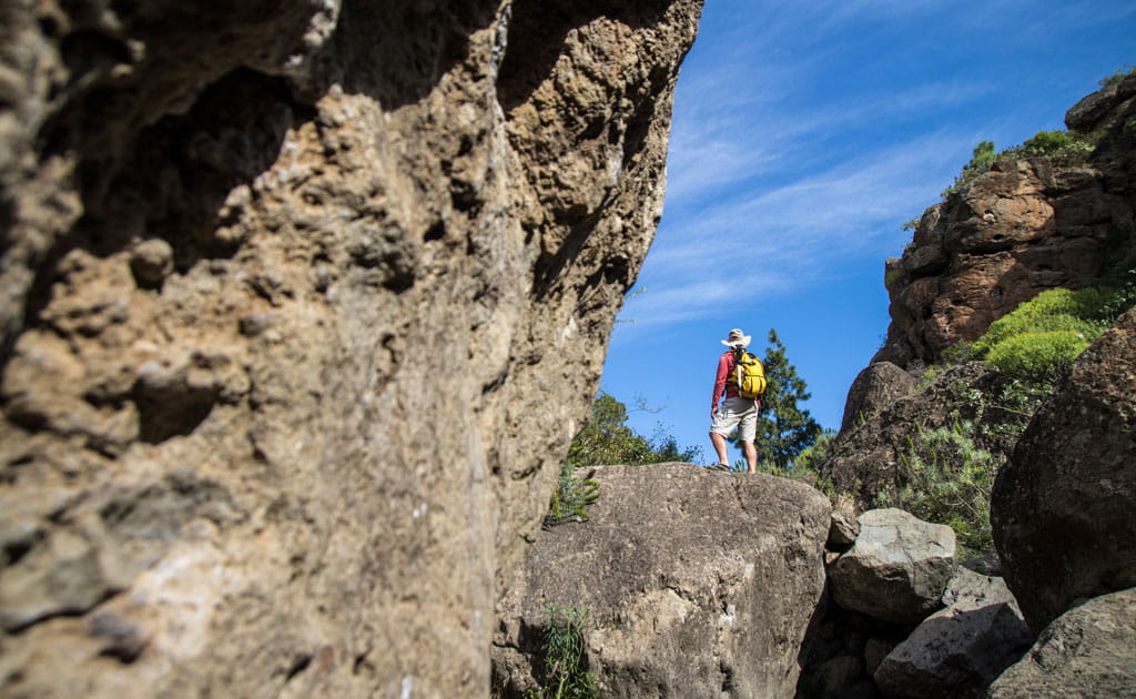 Person mit gelbem Rucksack auf einem felsigen Pfad auf Teneriffa unter blauem Himmel.