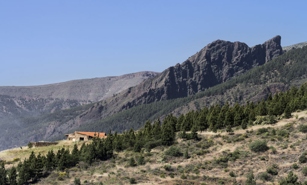 Landhaus vor Bergen und Wald auf Teneriffa bei klarem Himmel.