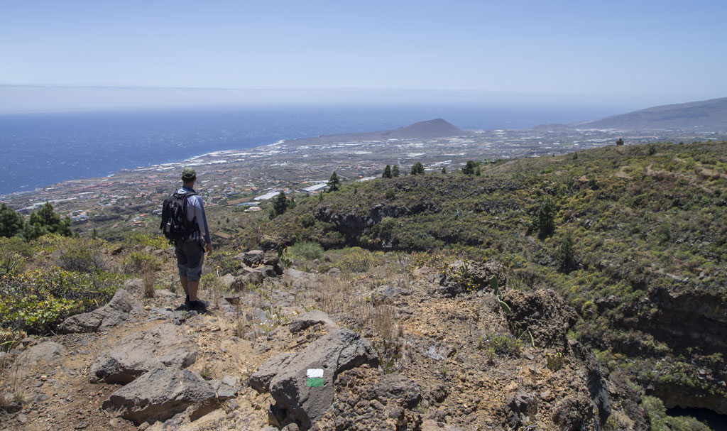 Person, die auf einem felsigen Weg mit Blick auf das Meer und die Landschaft von Teneriffa spaziert.