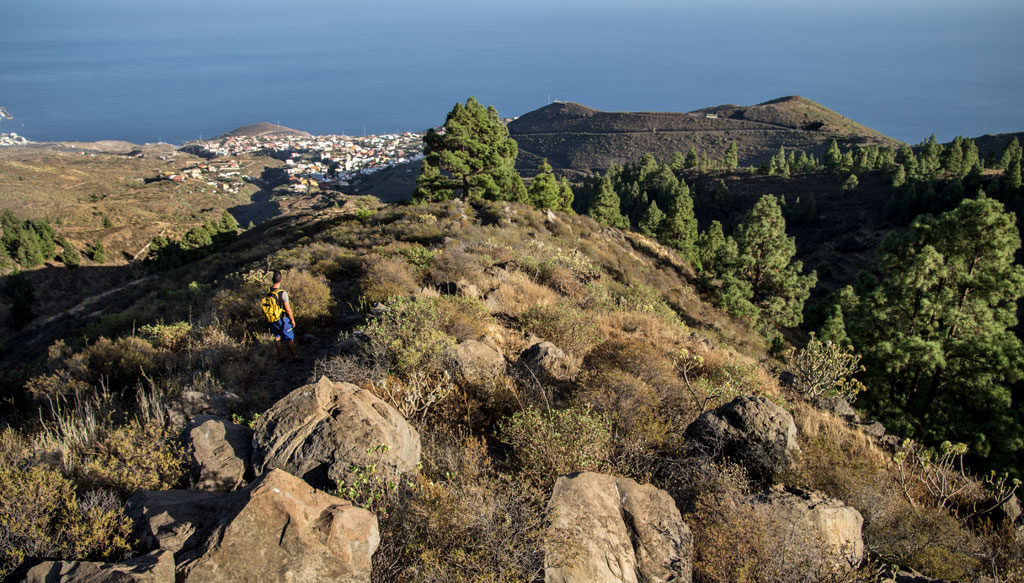 Bergiger Wanderweg auf Teneriffa mit Meeresblick und einem Wanderer mit Rucksack.