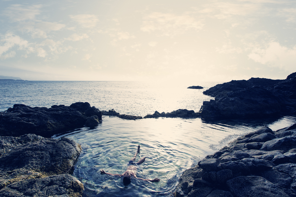 Person, die in einem natürlichen Becken, umgeben von Felsen am Ozean auf Teneriffa, schwimmt.
