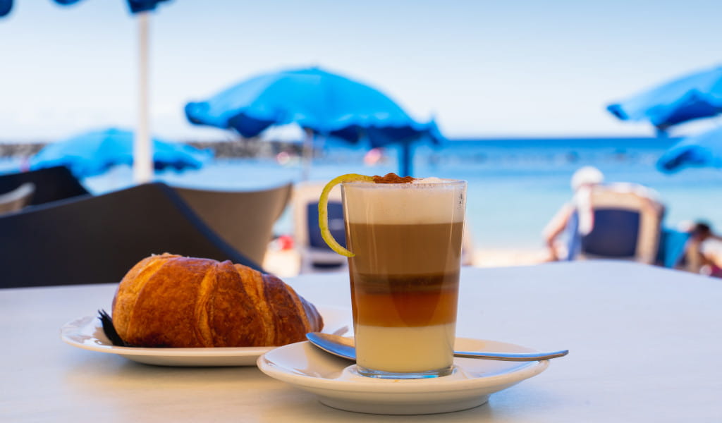 Barraquito-Kaffee und Croissant am Meer auf Teneriffa.