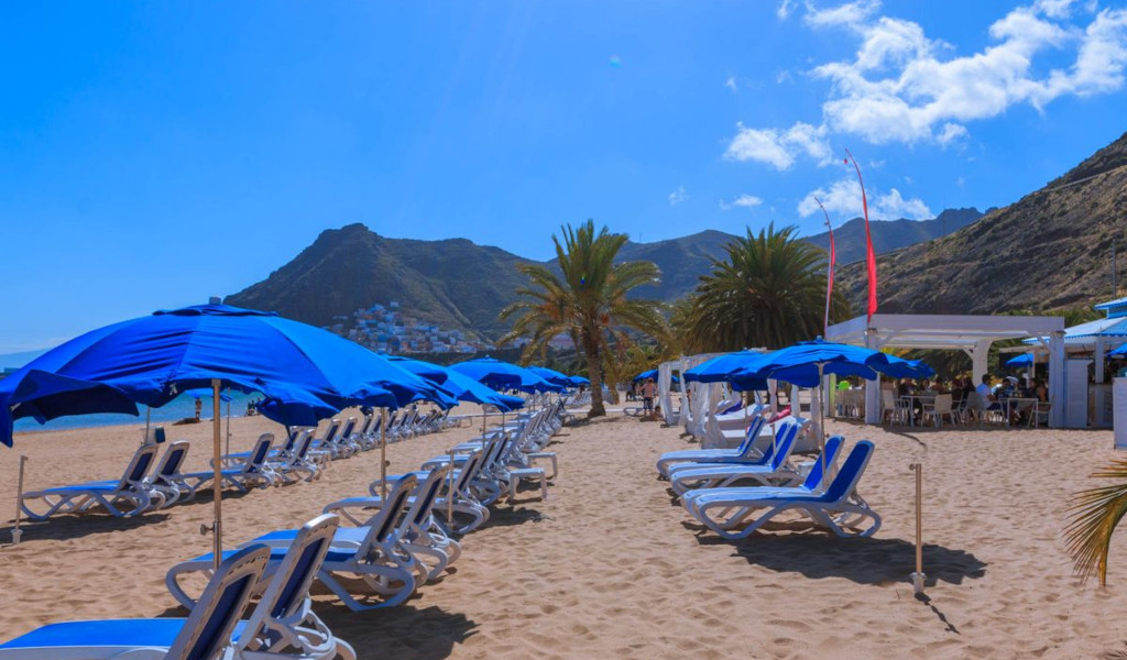 Liegeplätze und blaue Sonnenschirme am Strand Las Teresitas auf Teneriffa.