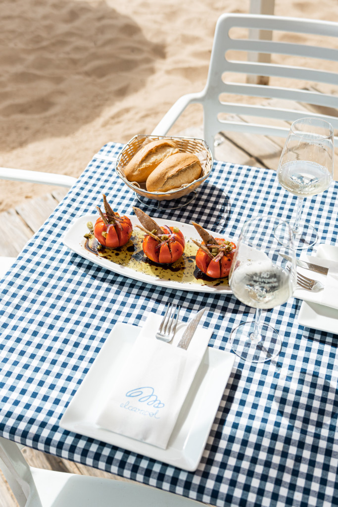 Tisch mit gefüllten Tomaten, Brot und einem Glas Wein vor dem Strand El Ancla auf Teneriffa.