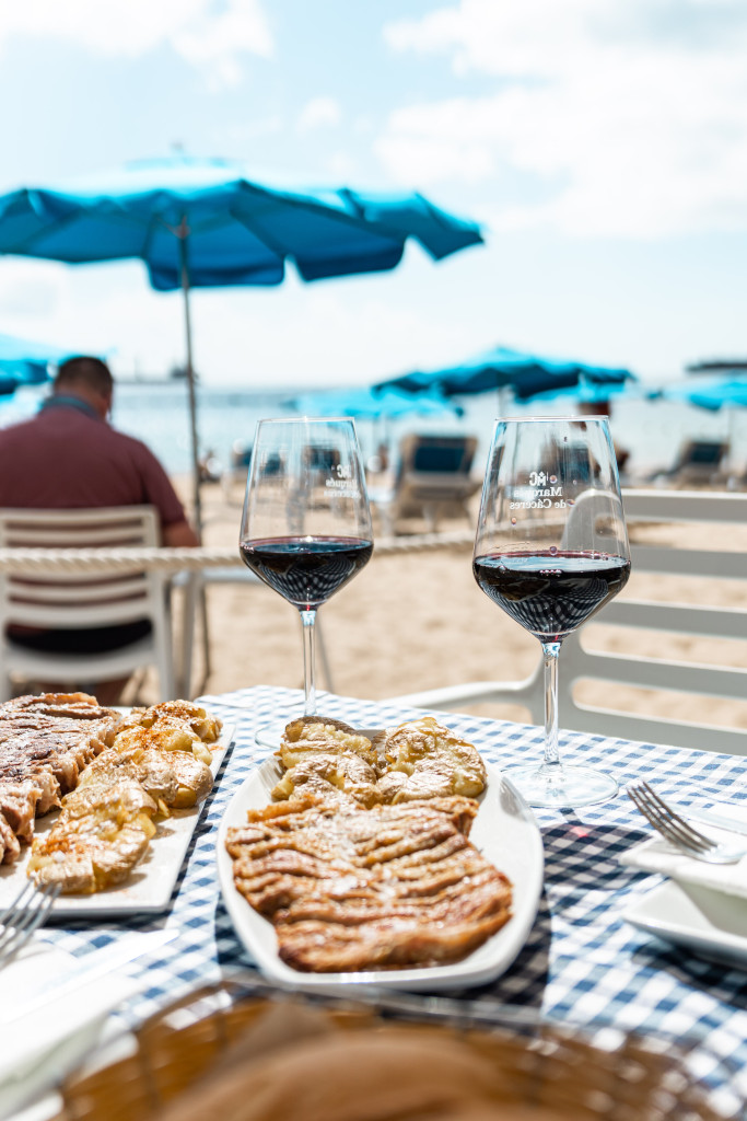 Gläser Wein und Essen am Strand mit blauen Sonnenschirmen auf Teneriffa.
