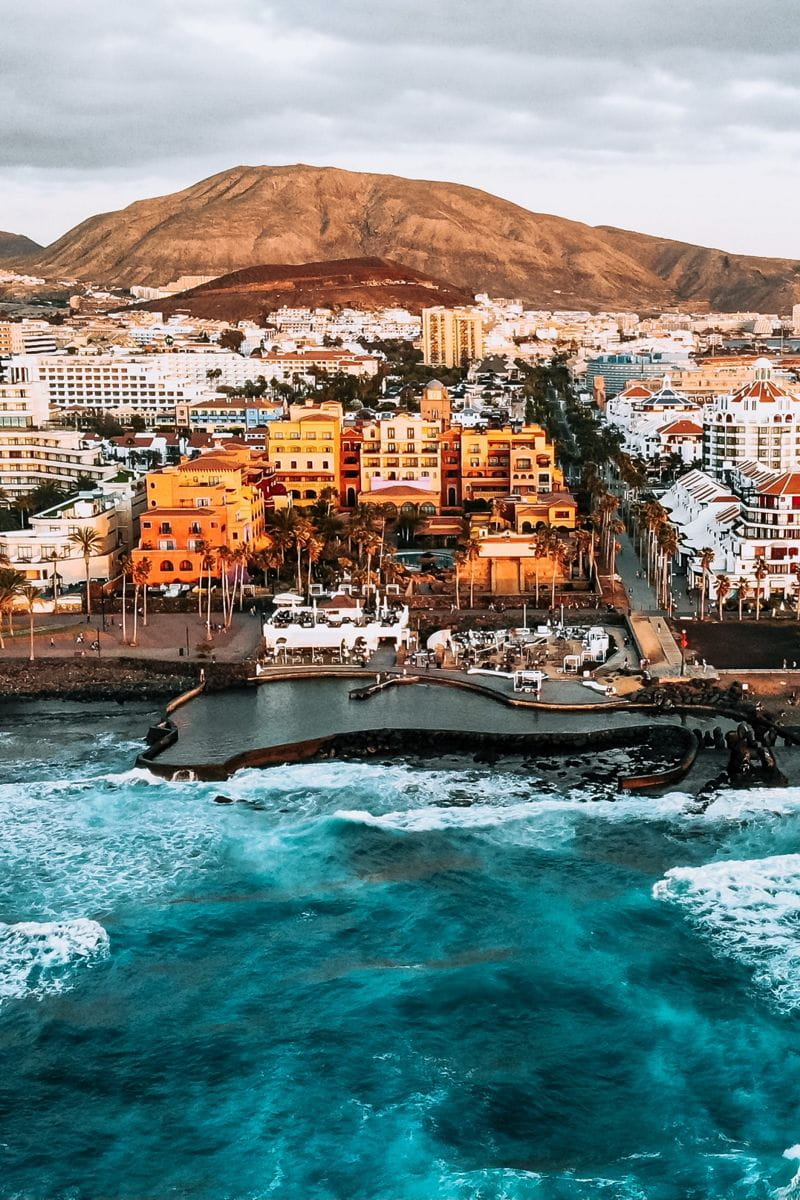 Luftaufnahme der Küste von Teneriffa mit Gebäuden und einem Berg im Hintergrund.