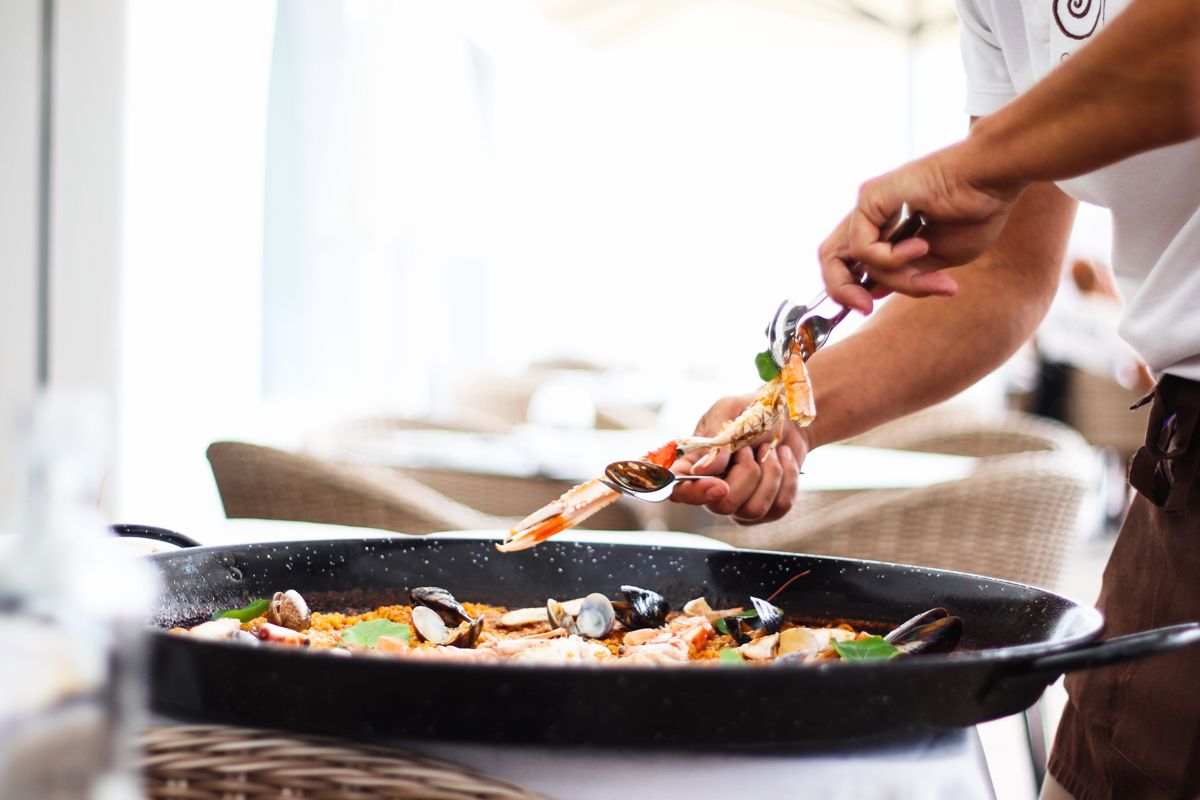 Person, die Meeresfrüchte in einer Paella auf einer Restaurantterrasse auf Teneriffa serviert.