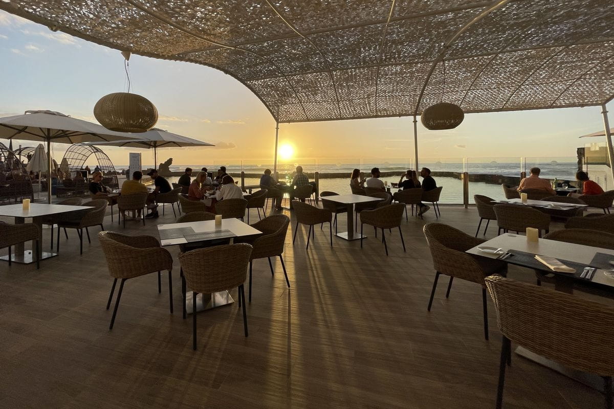 Menschen, die bei Sonnenuntergang auf einer Terrasse mit Blick auf das Meer auf Teneriffa speisen.