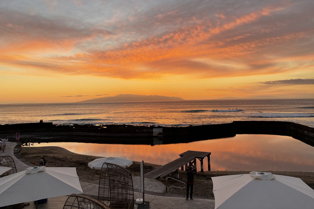 Sonnenuntergang über dem Ozean auf Teneriffa mit orangefarbenem Himmel und Schirmen im Vordergrund.