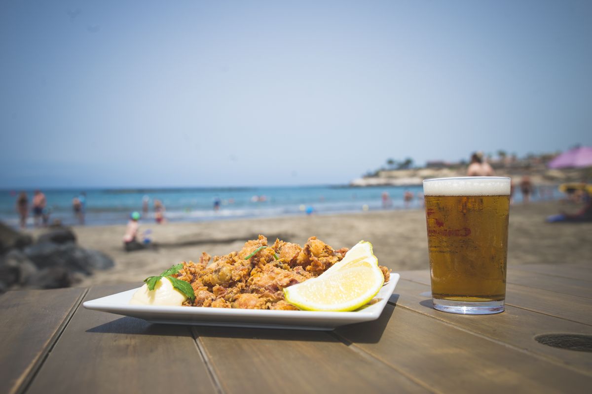 Teller mit Essen und ein Glas Getränk auf einem Tisch an einem Strand auf Teneriffa.