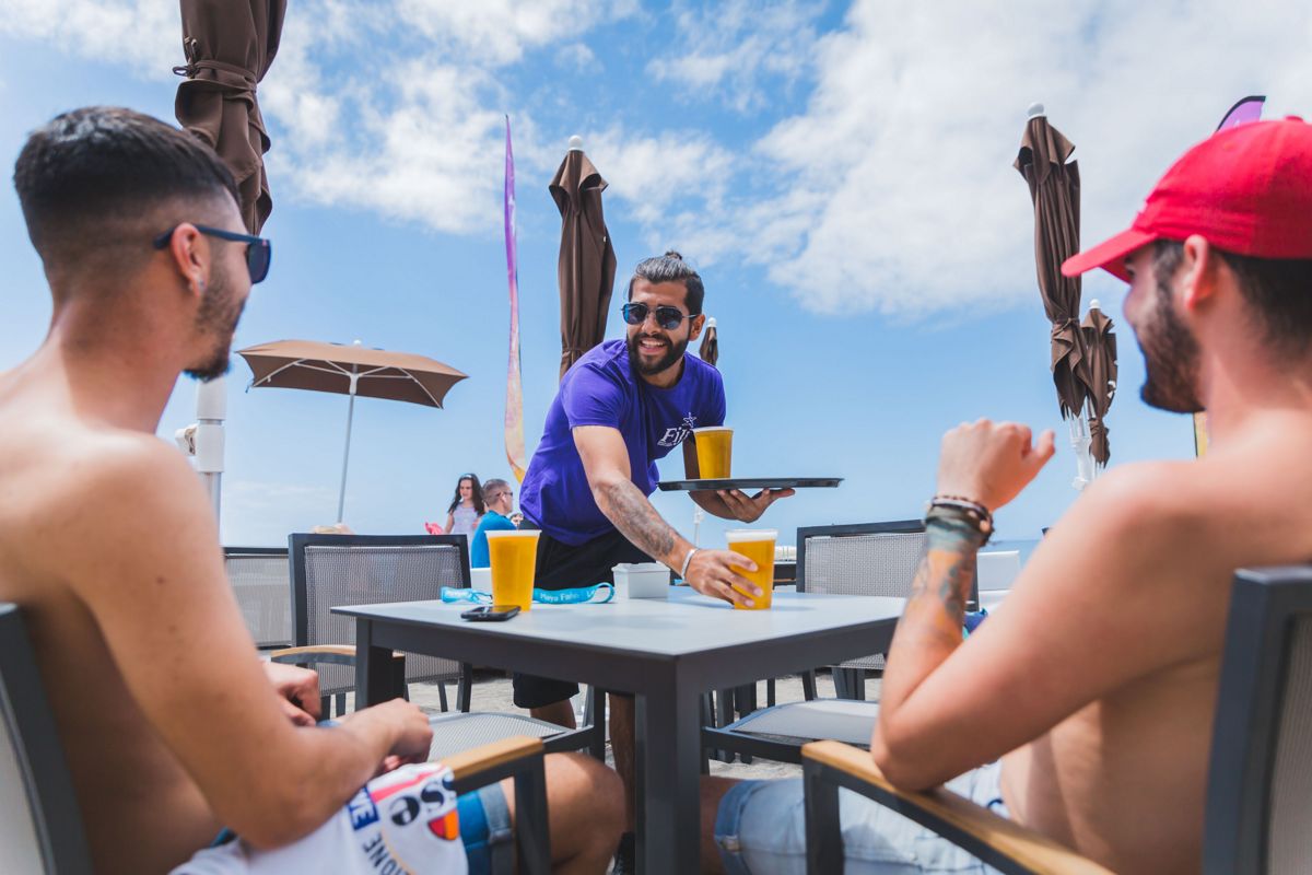 Kellner, der zwei Männern auf einer Terrasse auf Teneriffa Bier serviert.