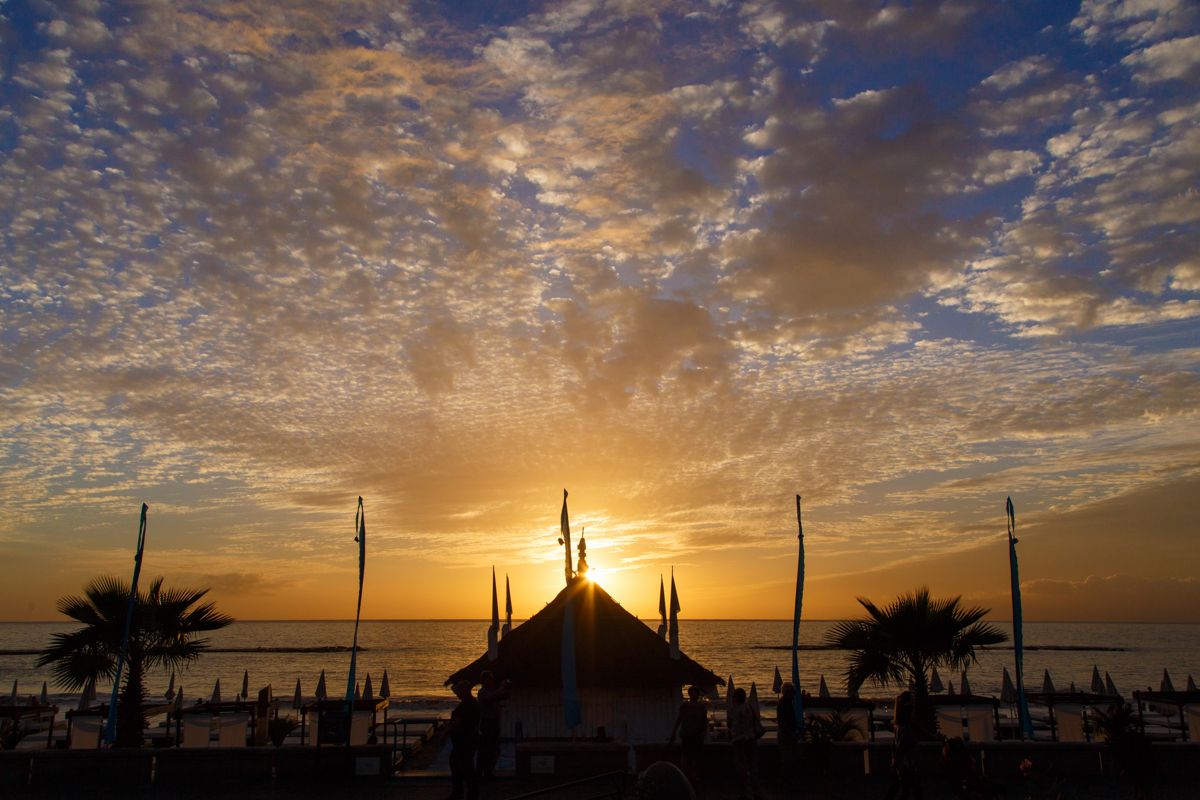 Sonnenuntergang am Strand mit Sonnenschirmen und Palmen auf Teneriffa.